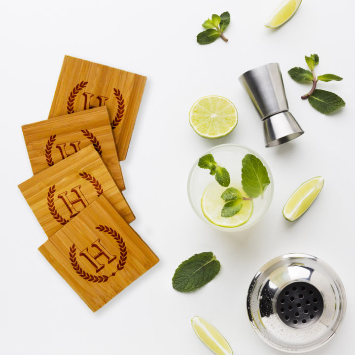 Bamboo coasters on top of white table next to mojito mixer and drink