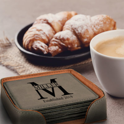 Personalized Miller Design Square Leatherette Coaster Set of 6 on table next to cup of coffee and crossaint